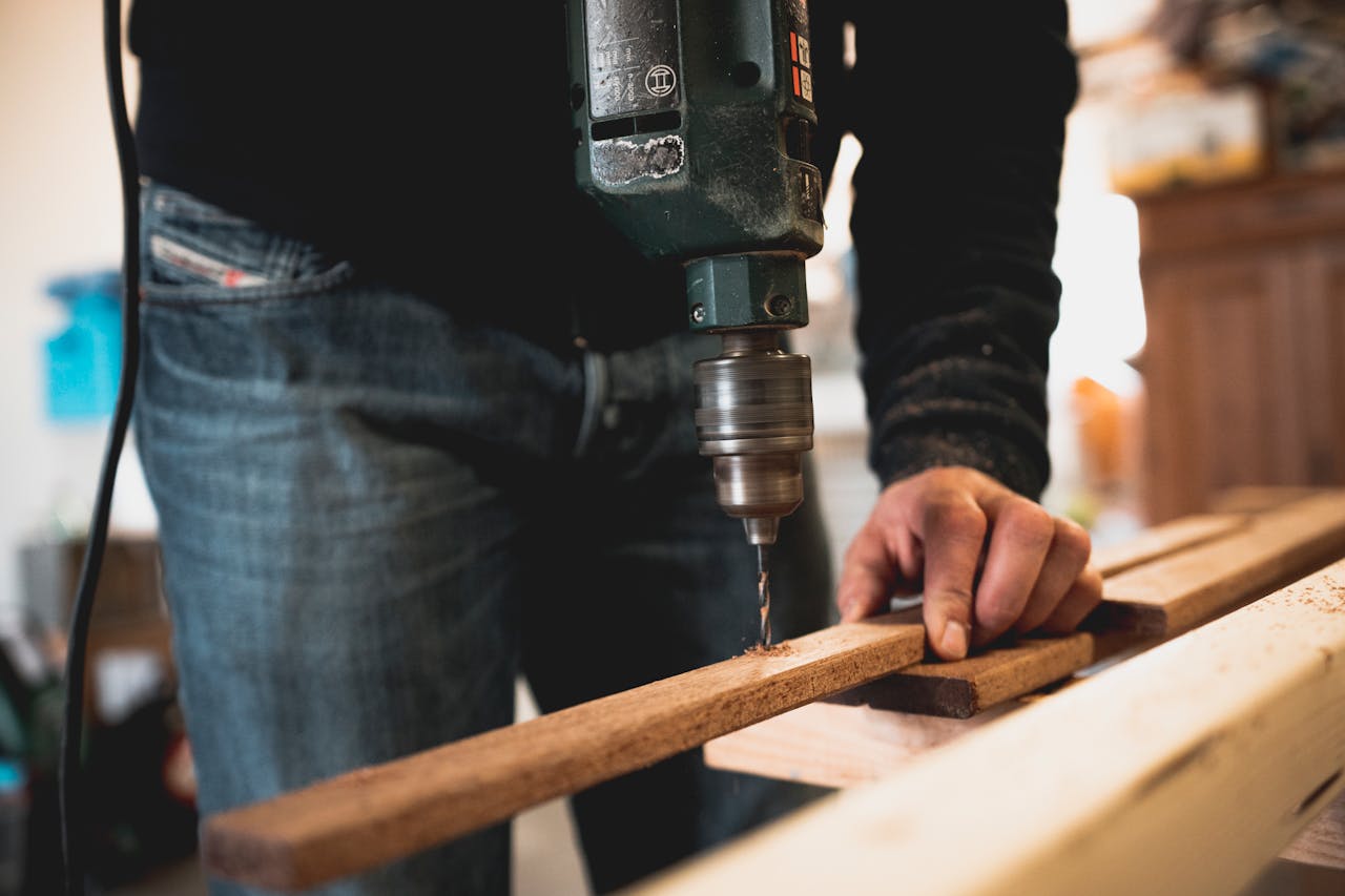services-02 Close-up of a person using an electric drill on a wooden plank, showcasing detailed woodworking skills.